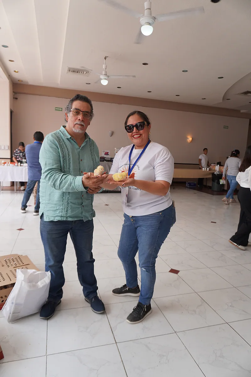 Expositor y asistente sostienen pollitos mientras miran a la cámara.