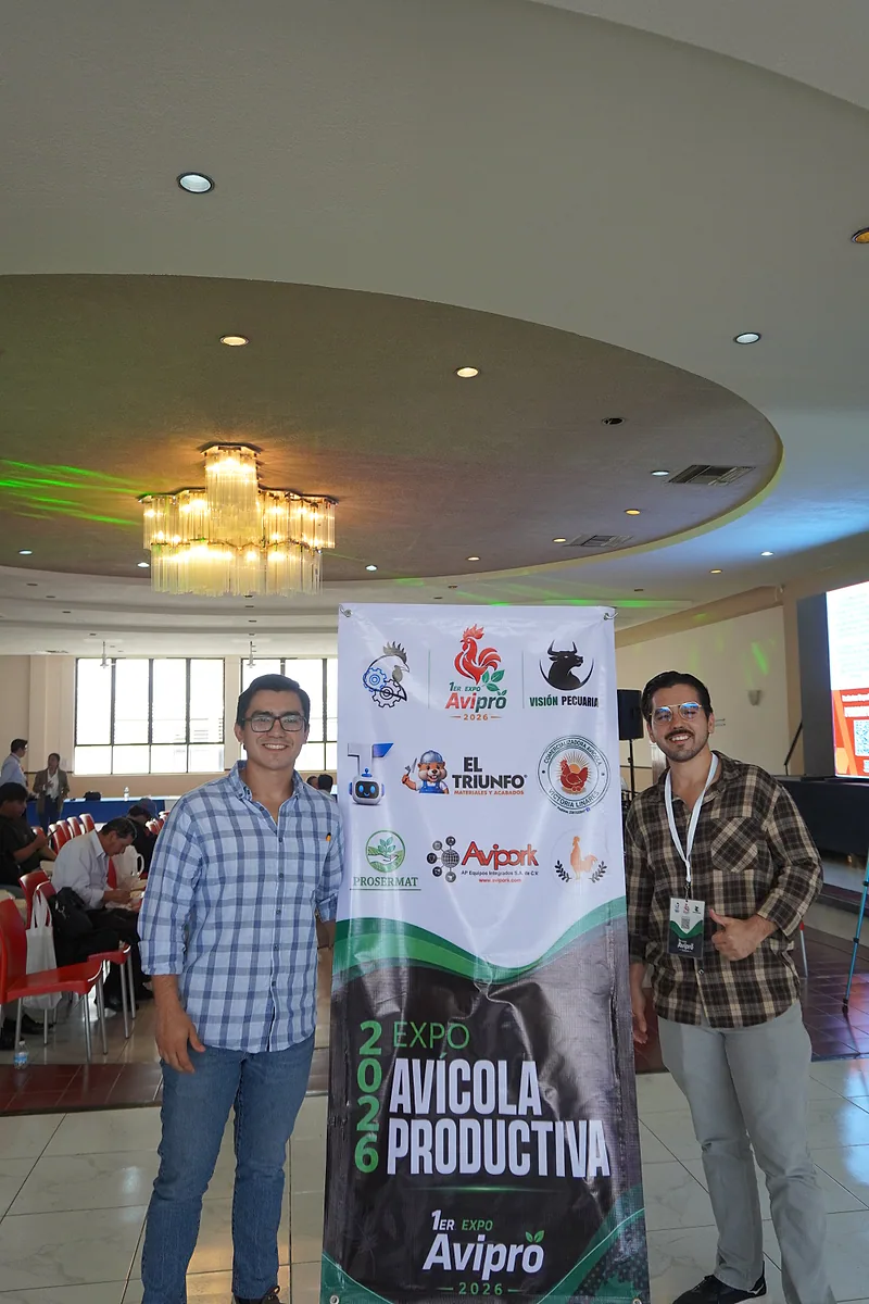 Dos asistentes sonríen junto al muro de identidad y patrocinadores de la Expo.